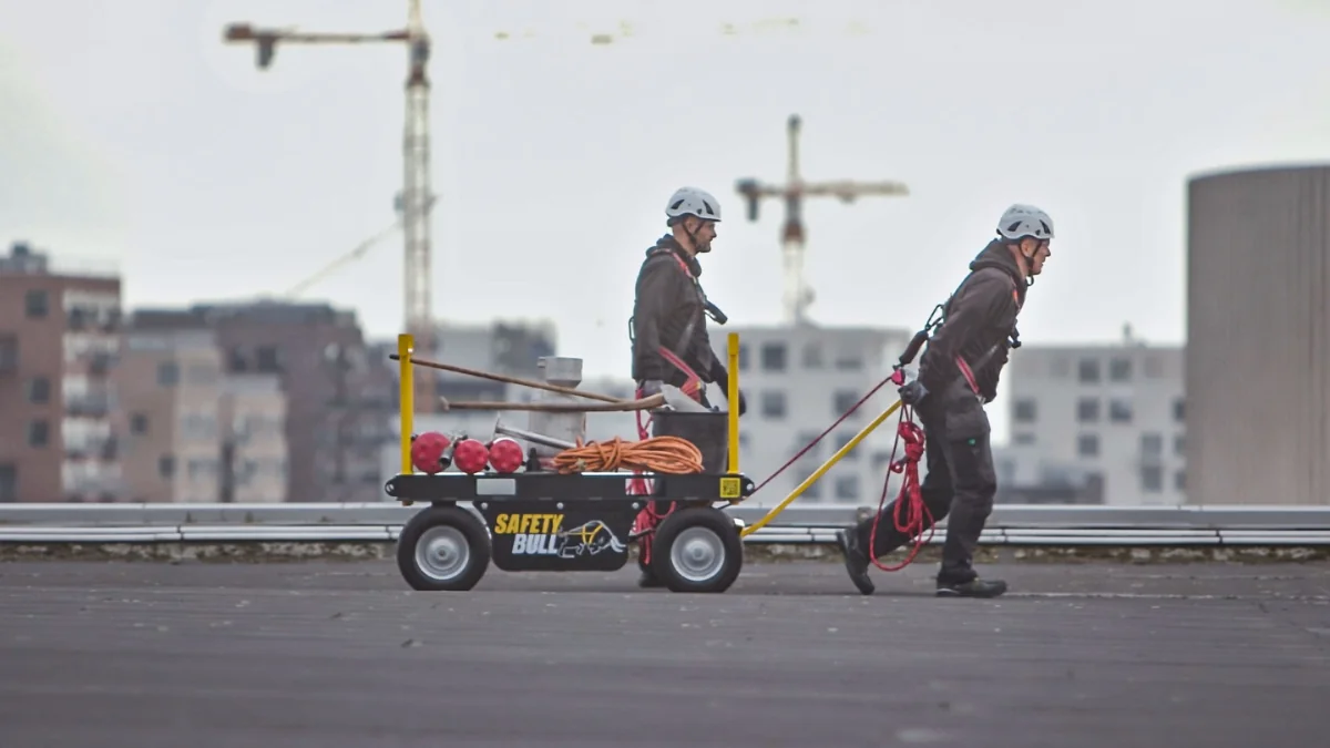 Roofing workers moving a Safety Bull mobile cart across a rooftop