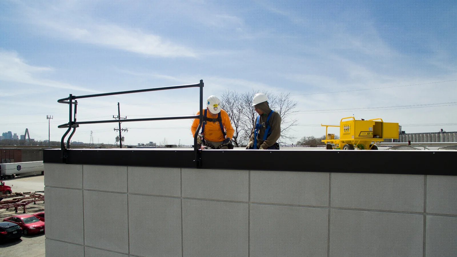 Two workers at a rooftop guardrail with a yellow LES cart nearby